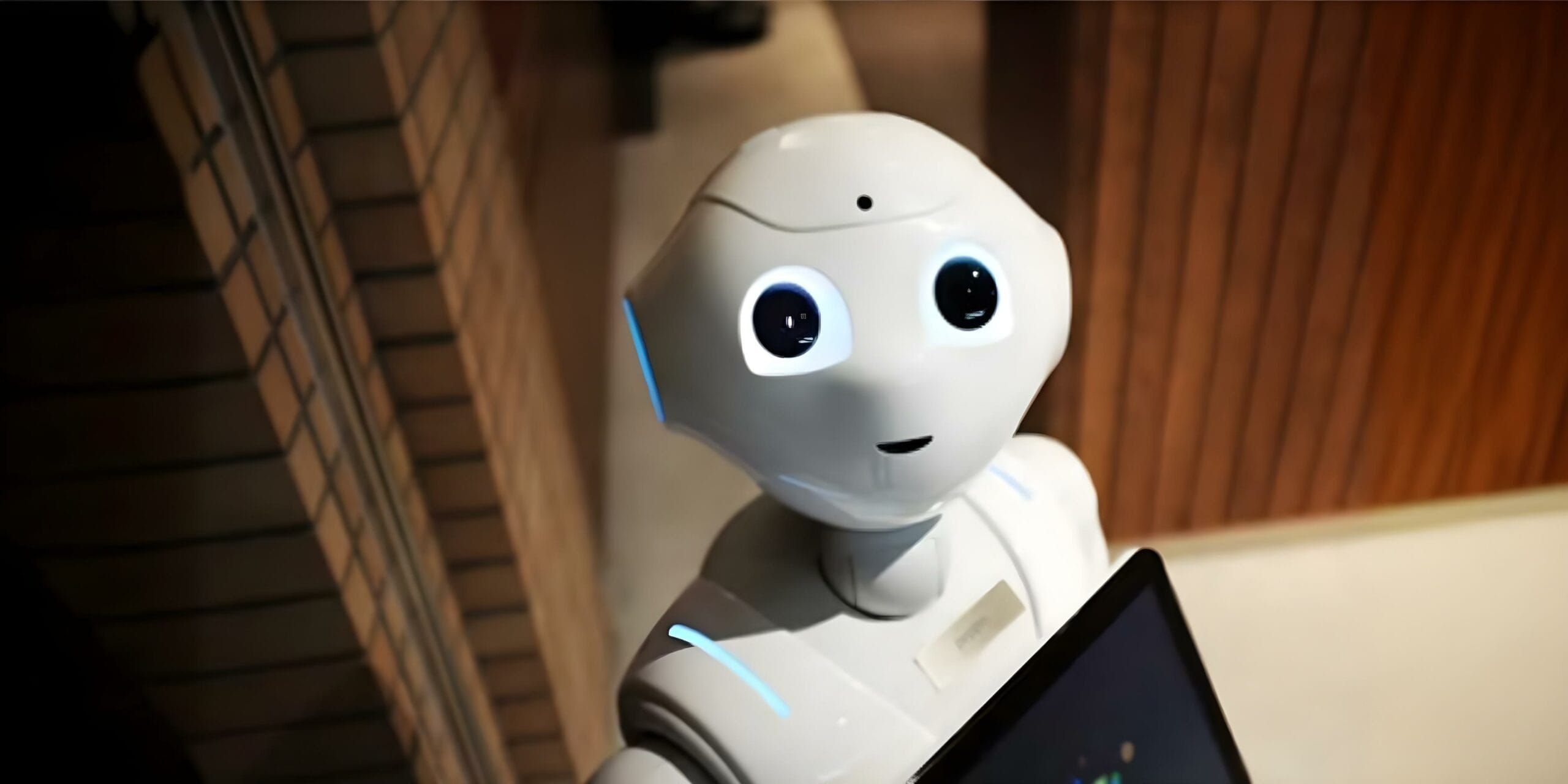 Humanoider Roboter mit großen, leuchtenden Augen blickt freundlich in die Kamera, moderne Umgebung im Hintergrund.